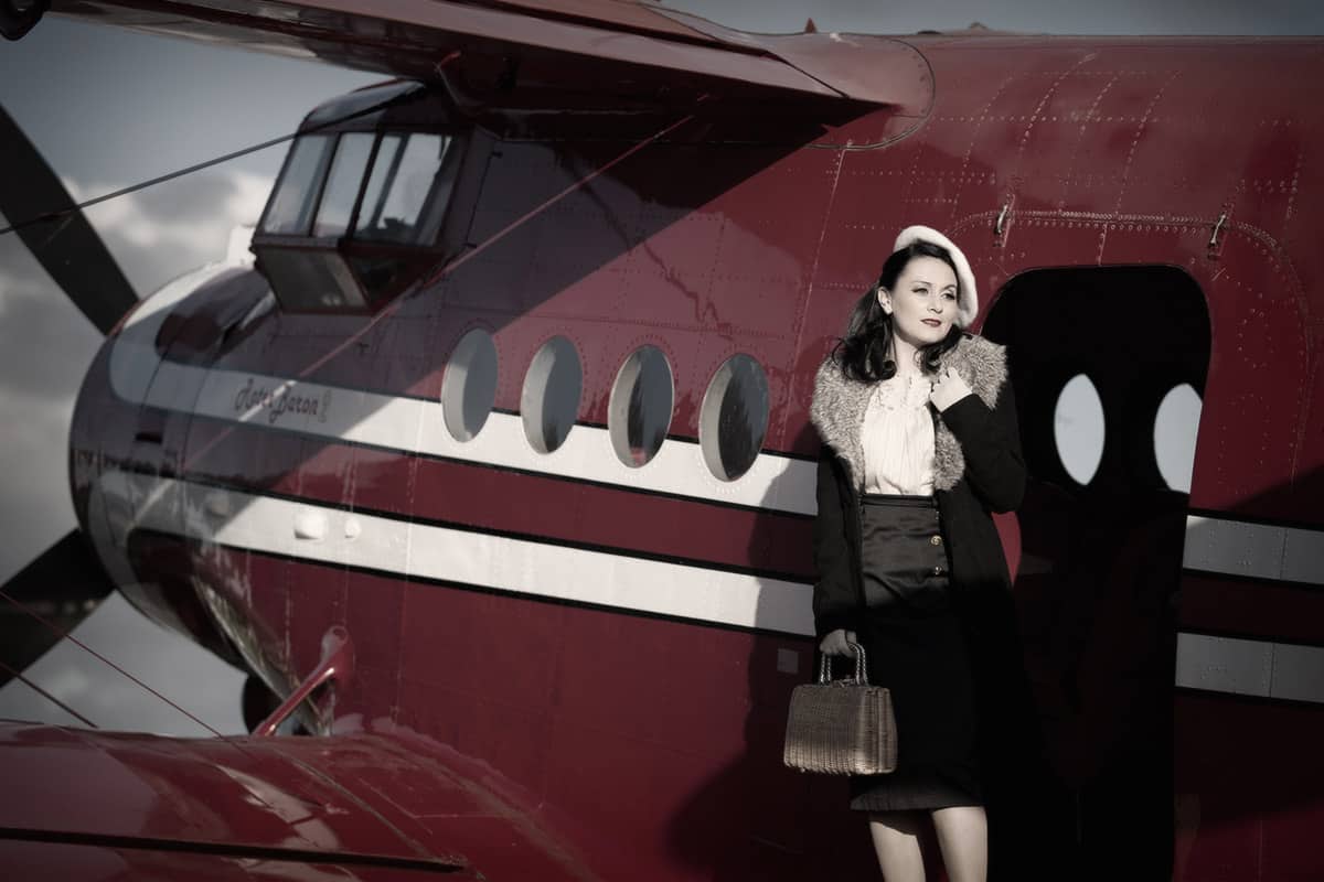 Eine junge Frau in Vintage-Kleidung betritt ein Doppeldecker-Flugzeug