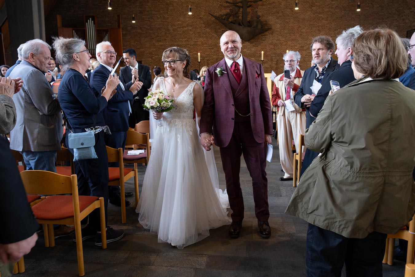 Das Brautpaar zieht Hand in Hand an den Gästen vorbei aus der Kirche